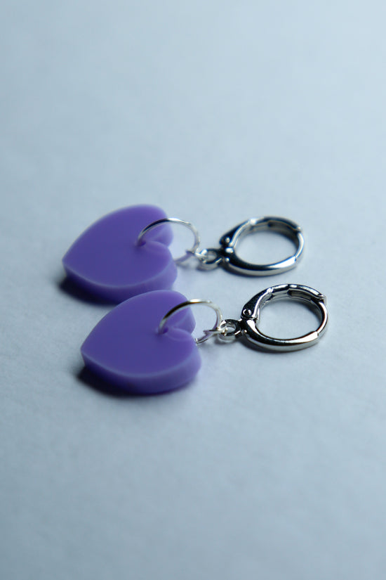 A pair of pastel purple star acrylic earring on a blue background