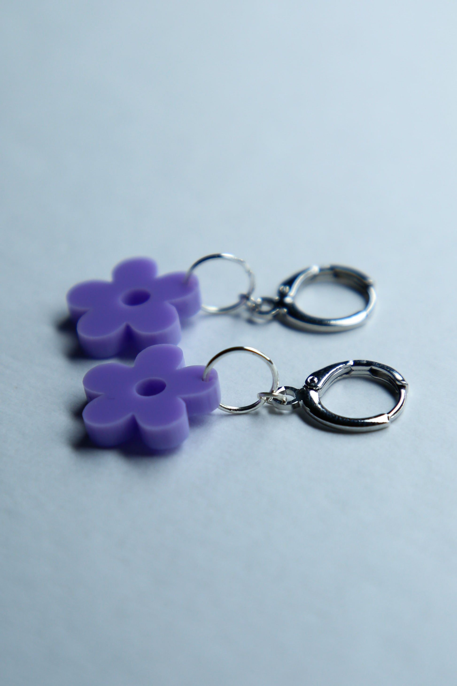 A pair of pastel purple flower acrylic earring on a blue background