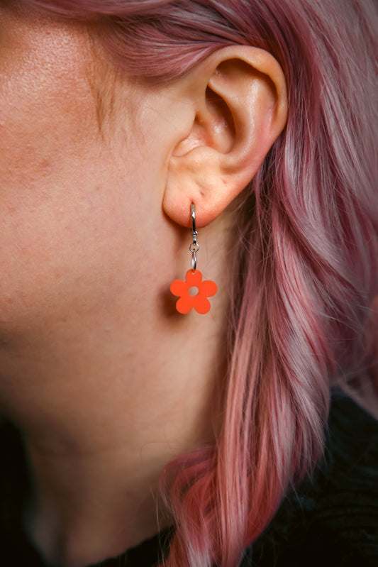 A pastel orange flower acrylic earring on an ear