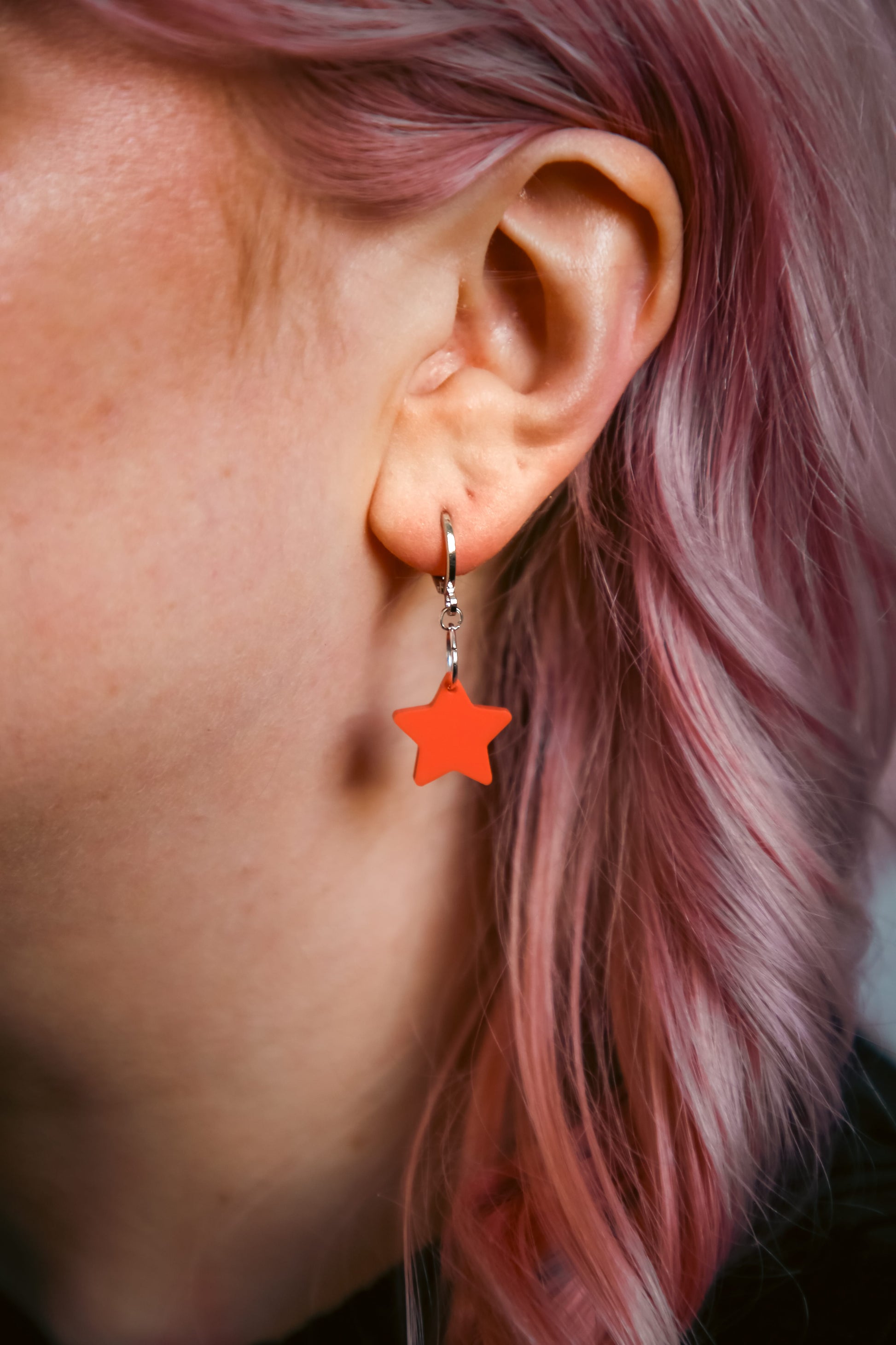 A pastel orange star acrylic earring on an ear