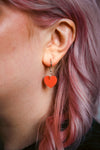A pastel orange heart acrylic earring on an ear