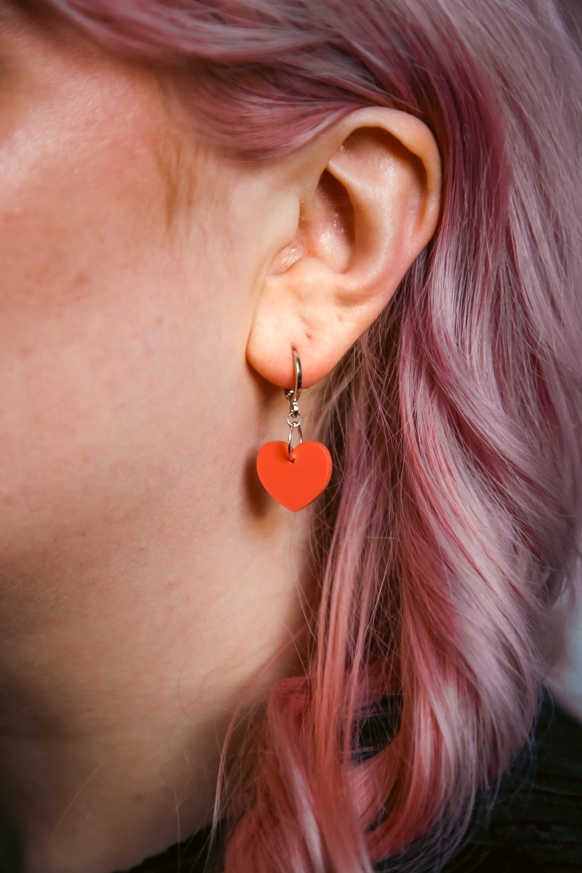 A pastel orange heart acrylic earring on an ear