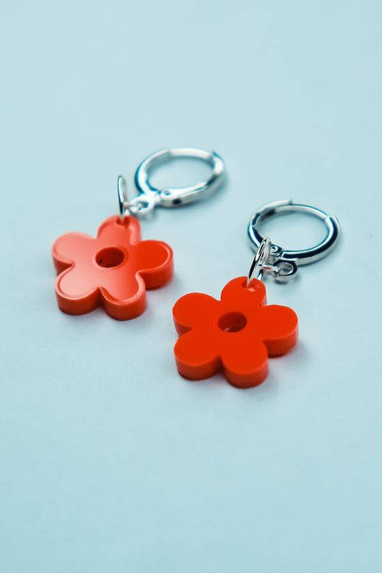A pair of pastel orange flower acrylic earring on a blue background