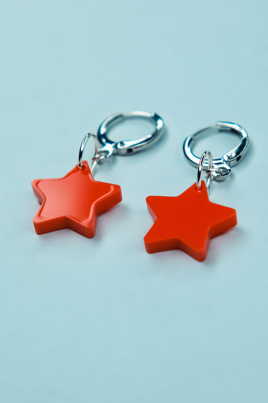 A pair of pastel orange star acrylic earring on a blue background