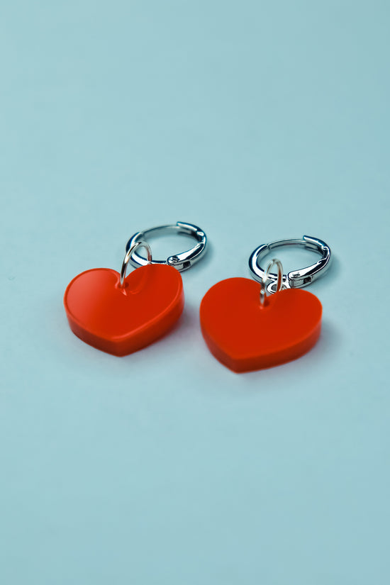 A pastel orange heart acrylic earring on a blue background