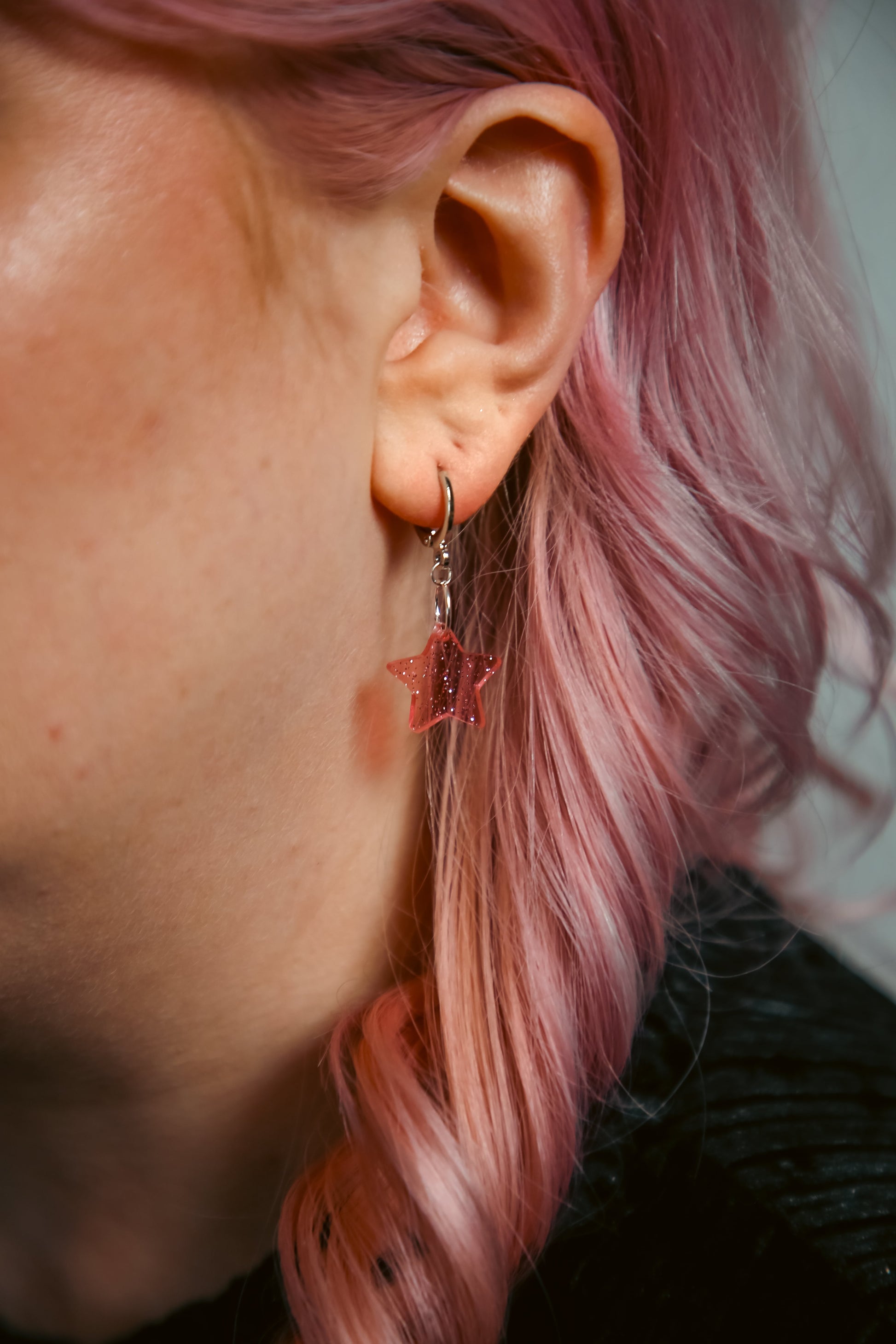 A transparent glitter pink star acrylic earring on an ear