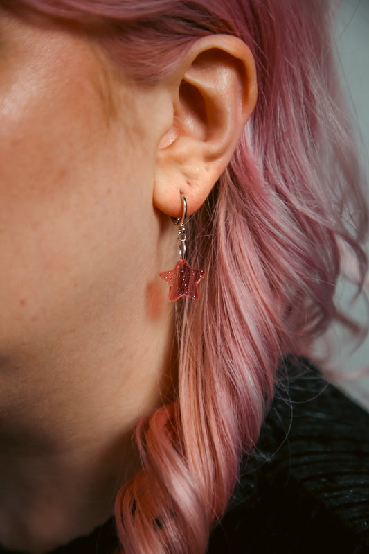 A transparent glitter pink star acrylic earring on an ear