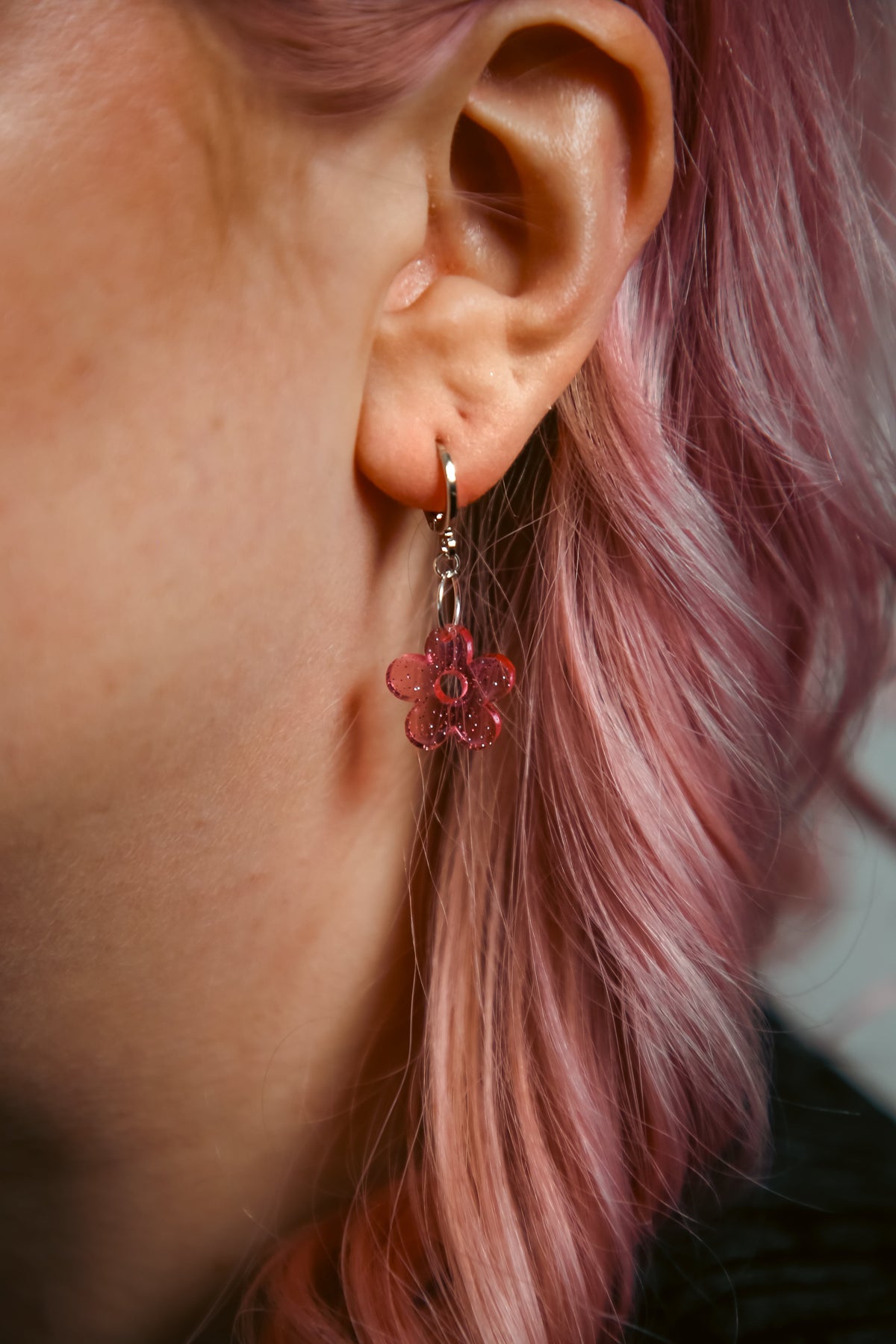 A transparent glitter flower acrylic earring on an ear