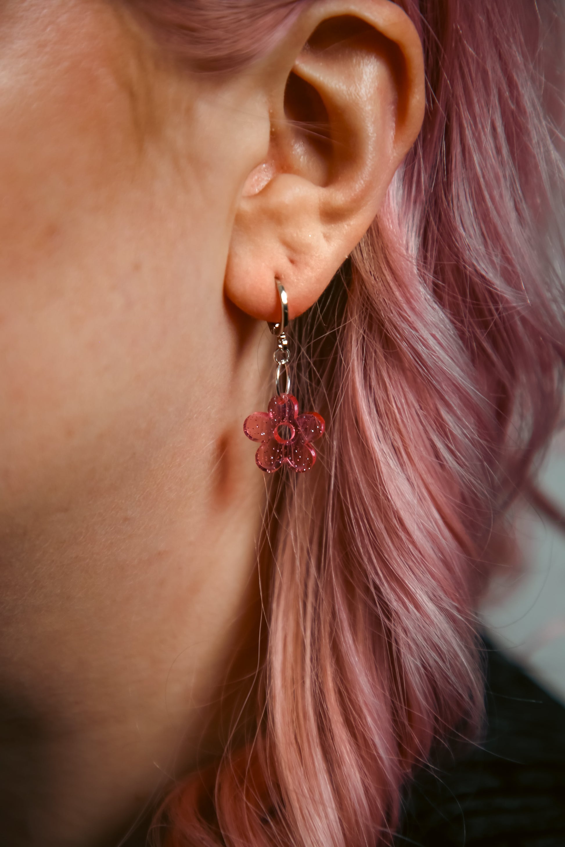 A transparent glitter flower acrylic earring on an ear