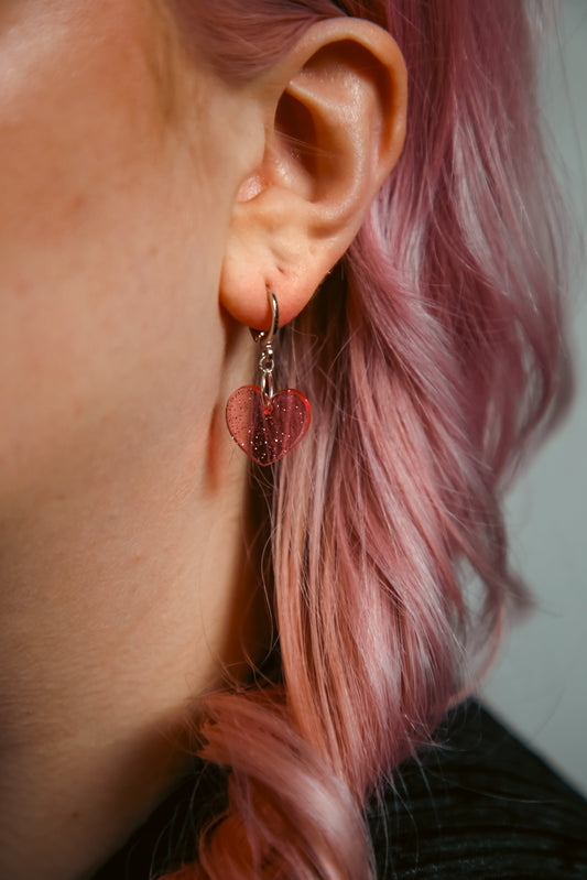 A pink transparent glitter heart acrylic earring on an ear