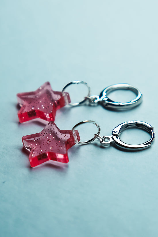 A pair of transparent glitter pink star acrylic earring on a blue background