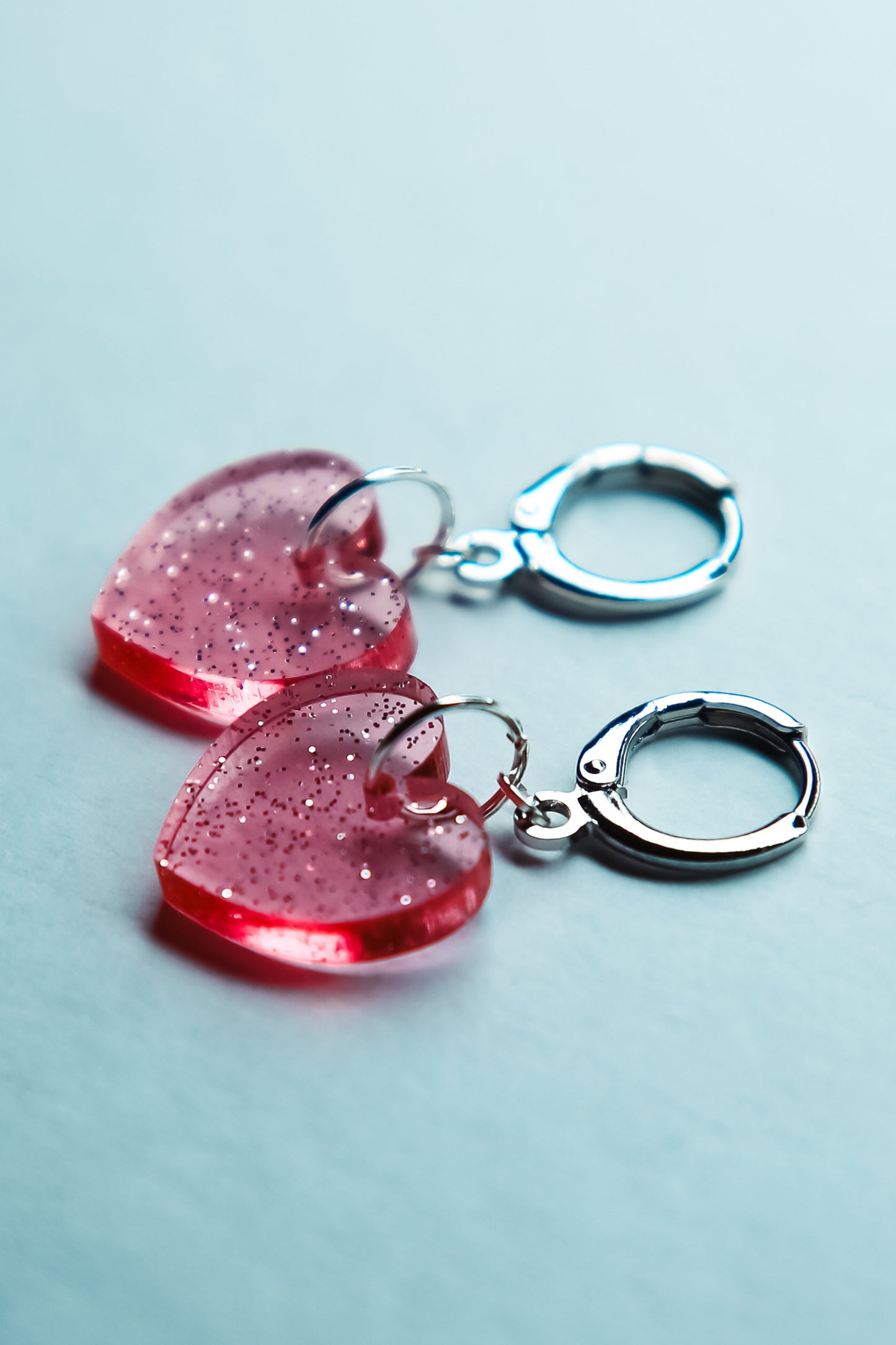 A pair of pink transparent glitter heart acrylic earring on a blue background