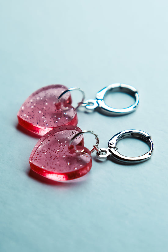 A pair of pink transparent glitter heart acrylic earring on a blue background