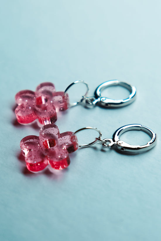 A pair of transparent glitter flower acrylic earrings on a blue background