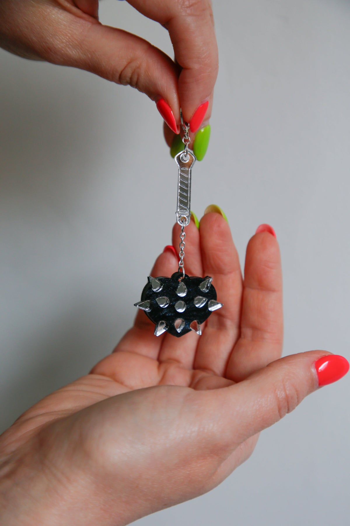 A mace weapon acrylic earring with a black love heart shaped ball and silver handle being held up