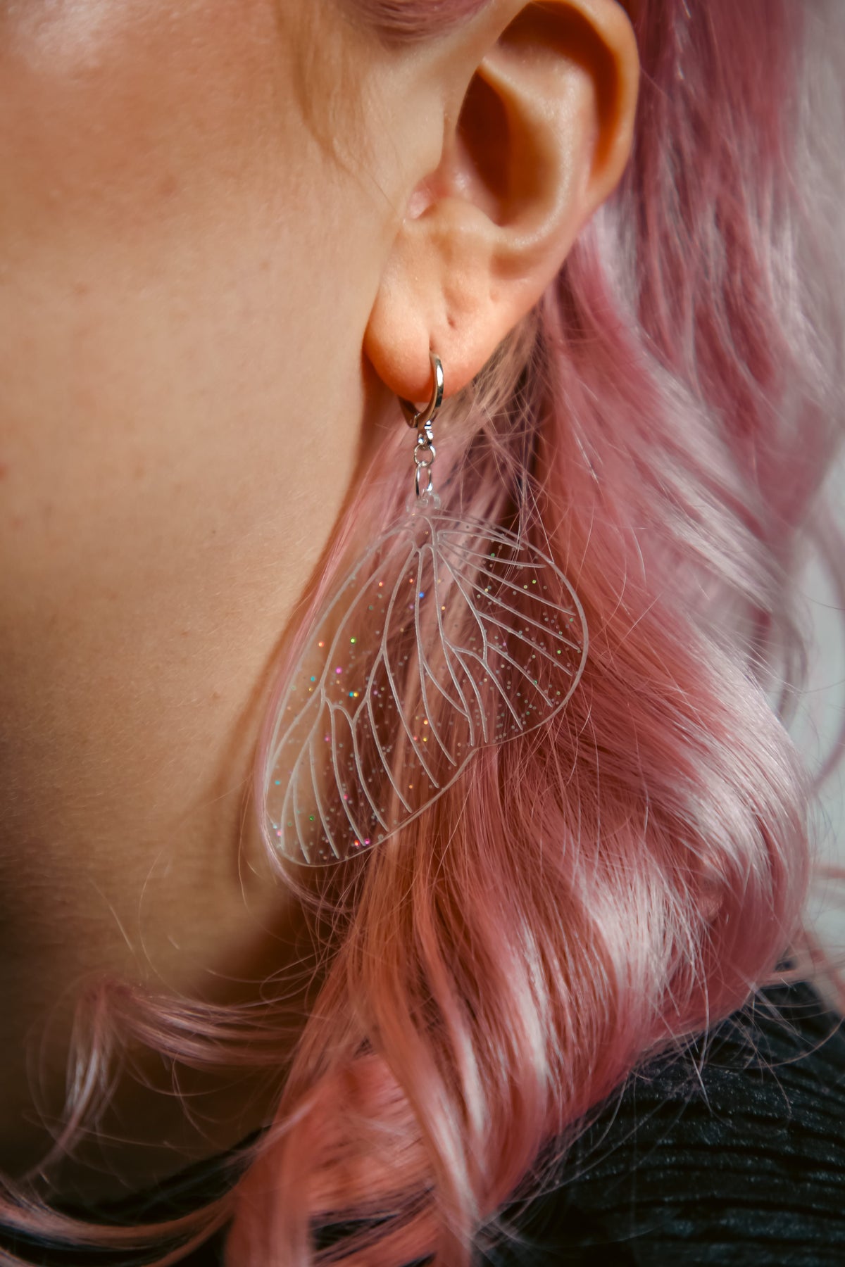 glitter transparent fairy wing earring on a persons ear with pink hair behind