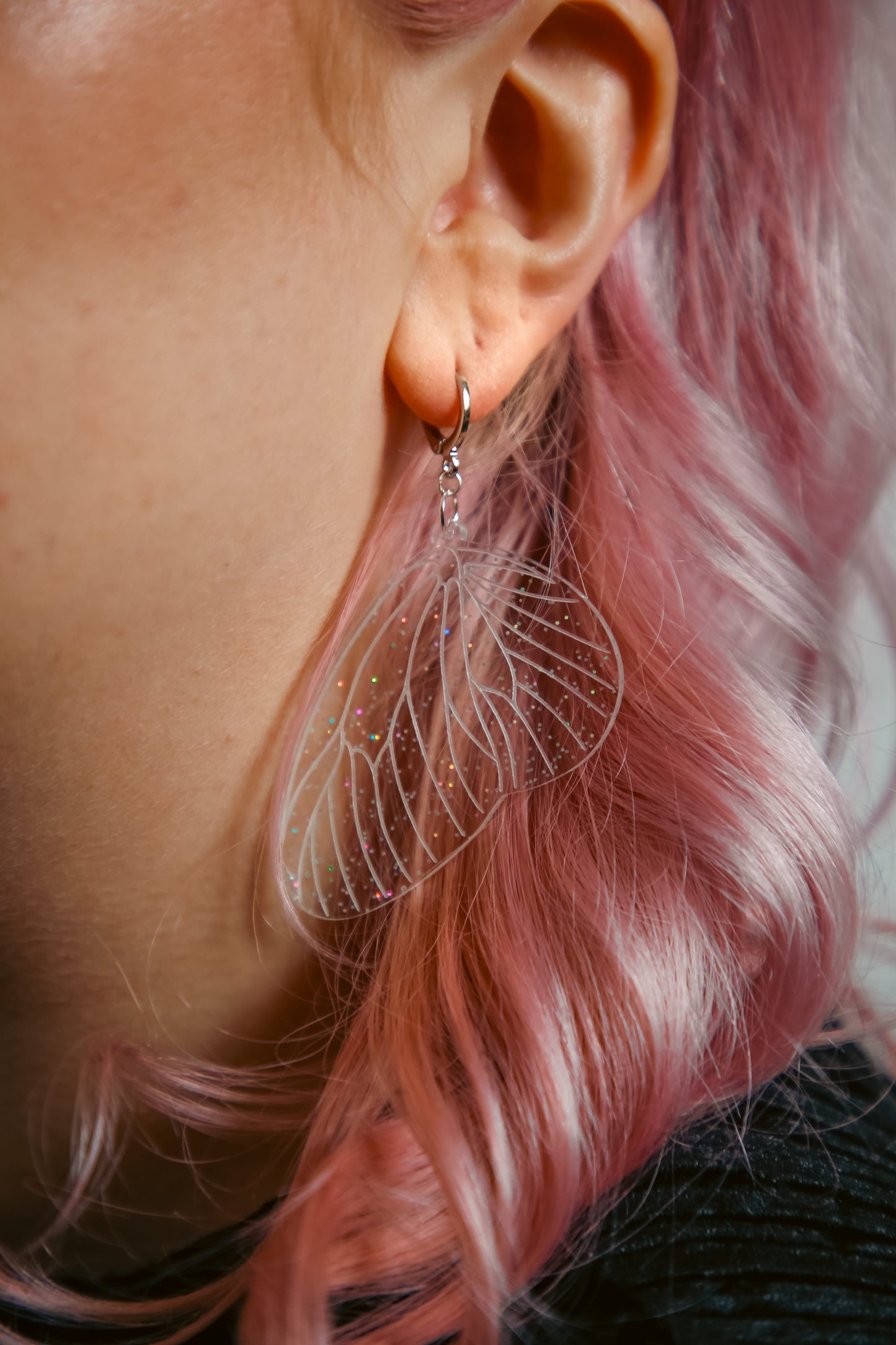 glitter transparent fairy wing earring on a persons ear with pink hair behind