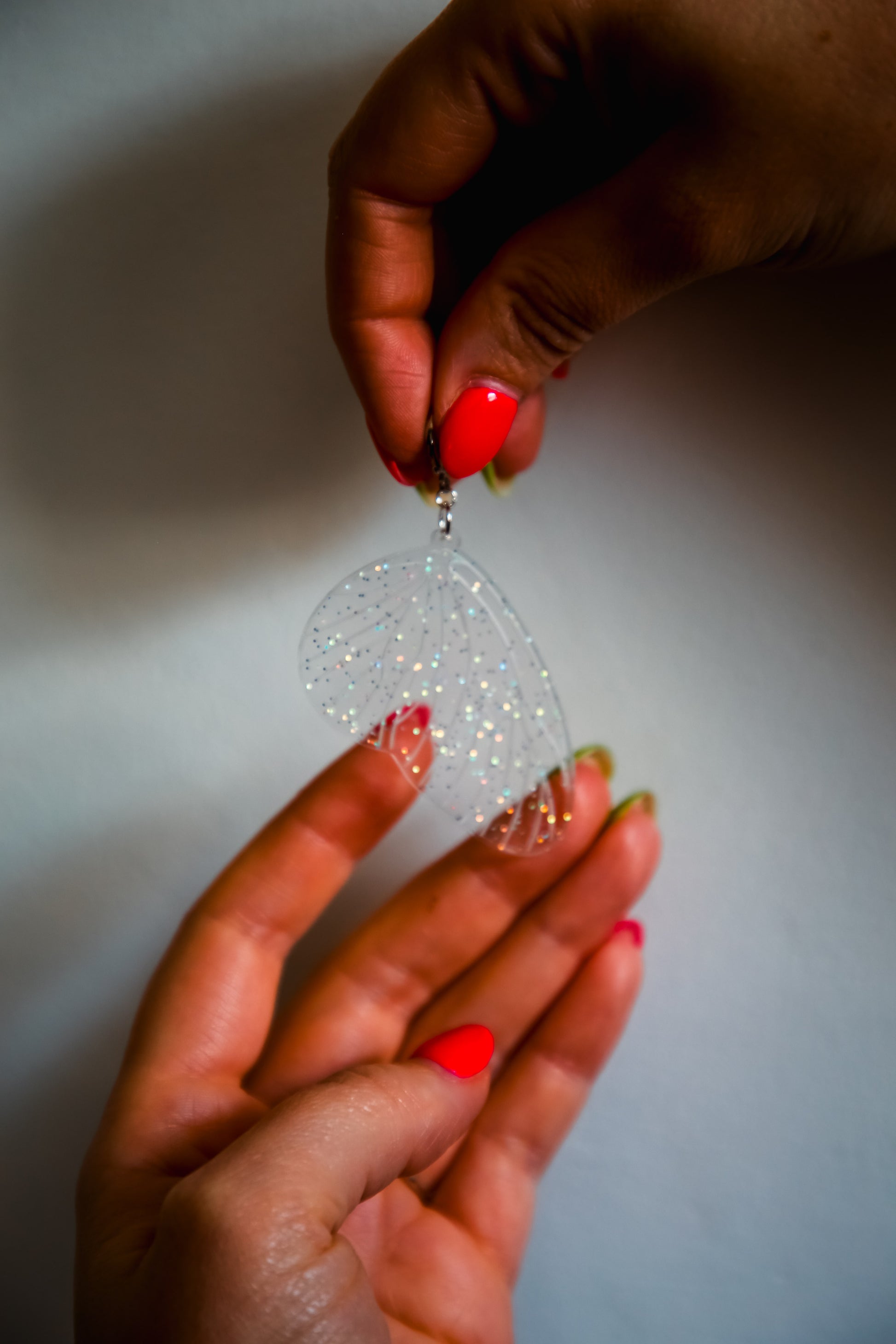 glitter transparent fairy wing earring being held by two hands