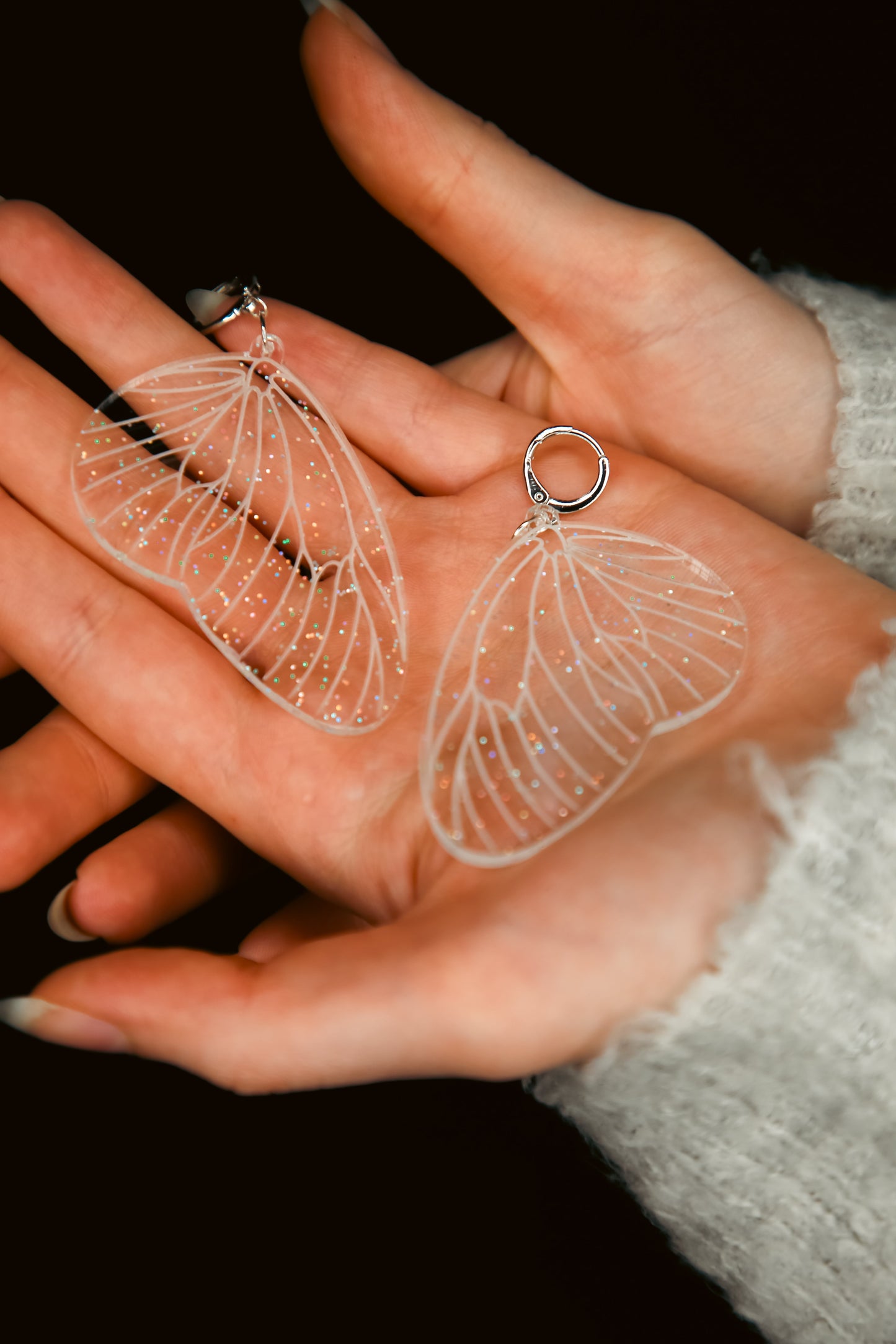 glitter transparent fairy wing earring on a persons ear with pink hair behind