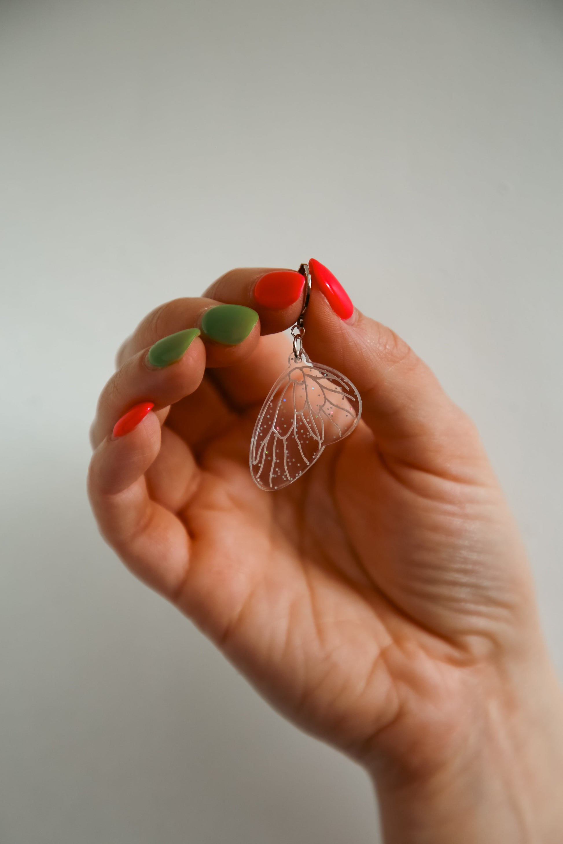 mini glitter transparent fairy wing acrylic earring being held by a persons hand