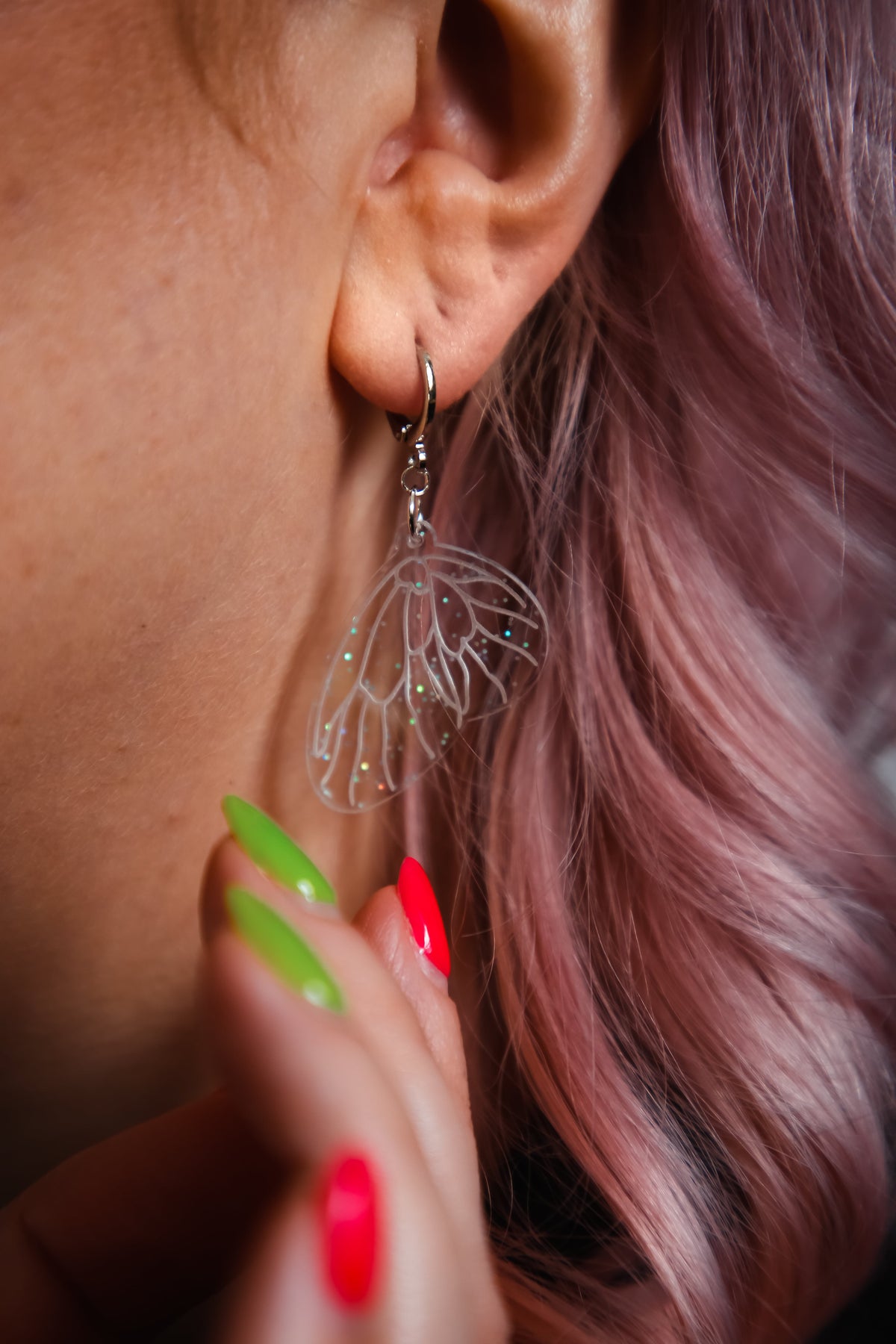 mini glitter transparent fairy wing acrylic earring on a persons ear with pink hair behind