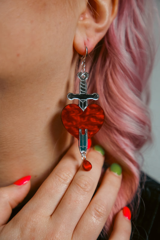 red and silver sword and heart acrylic earring being worn by a person with pink hair