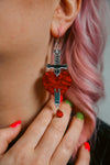 red and silver sword and heart acrylic earring being worn by a person with pink hair