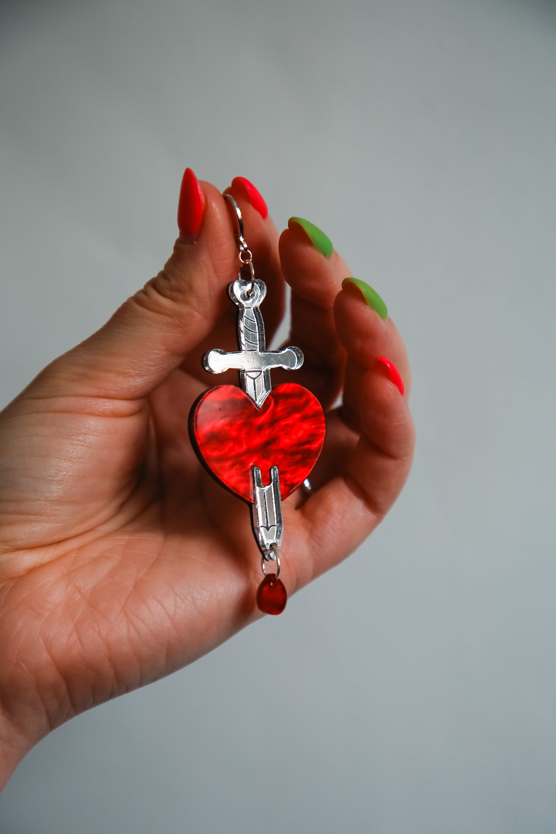 red and silver sword and heart acrylic earring being held by a hand