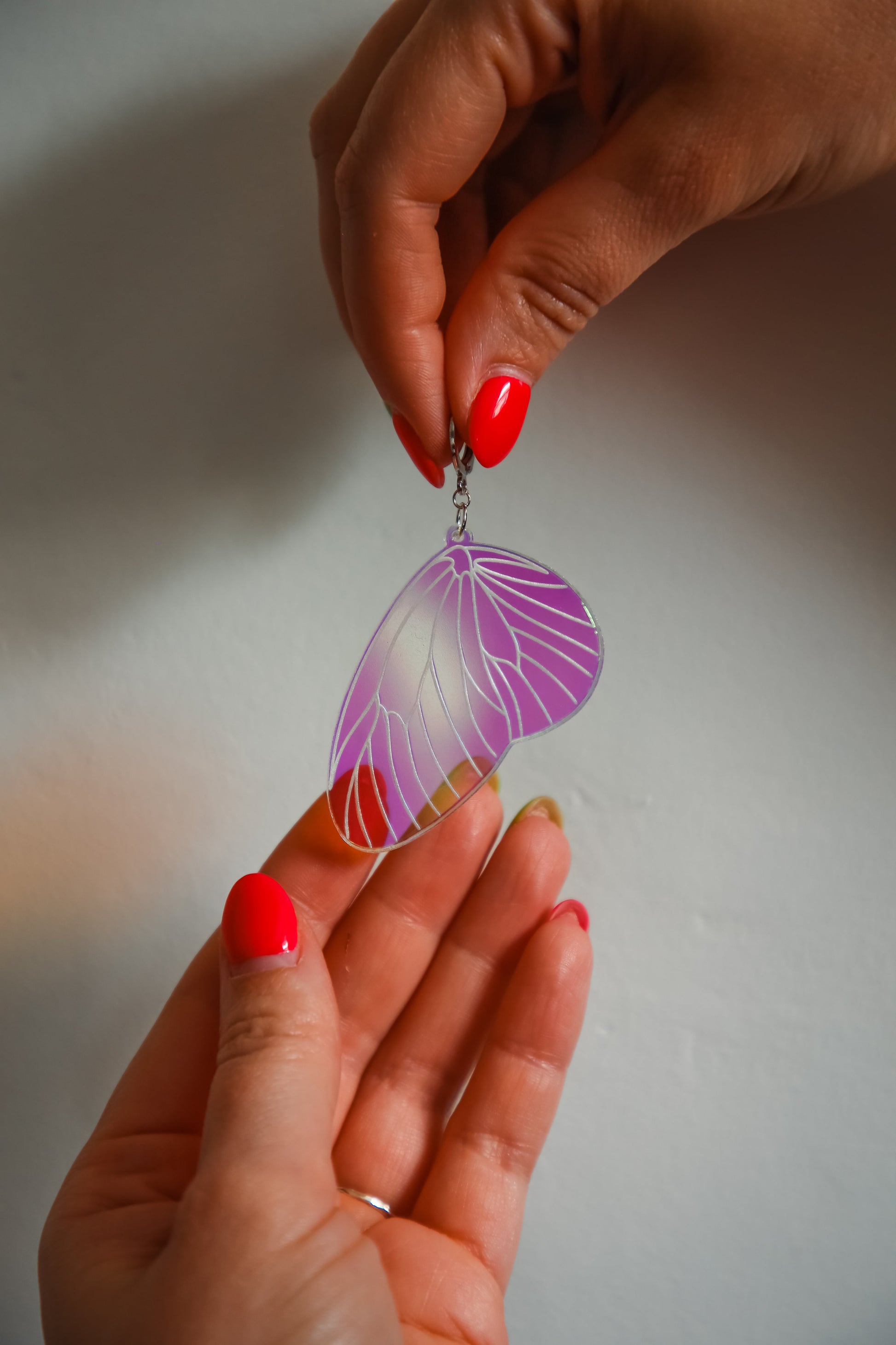 An iridescent acrylic earring styled after a fairies wing being held by hands