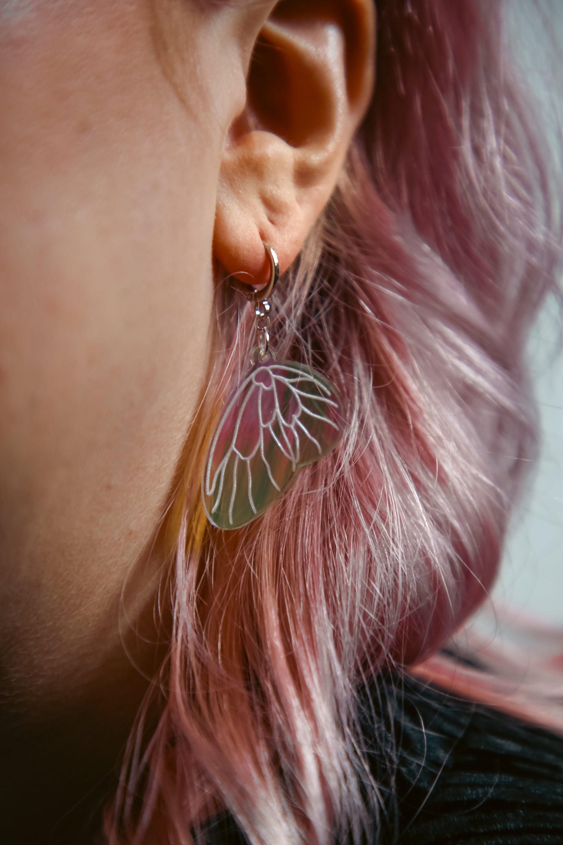 A mini iridescent acrylic earring styled after a fairies wing against pink hair