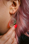 A mini iridescent acrylic earring styled after a fairies wing against pink hair