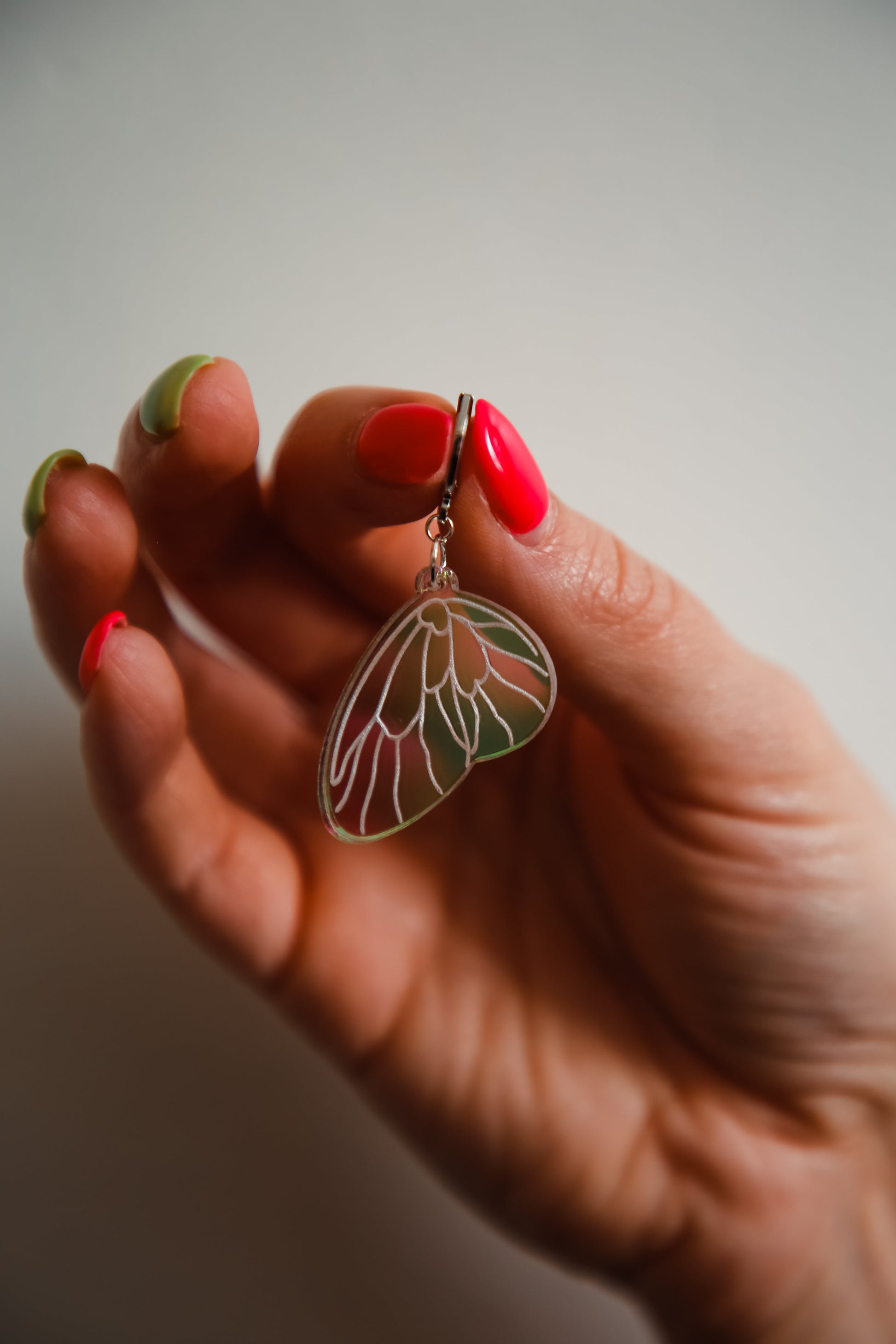 A small iridescent acrylic earring styled after a fairies wing being held up