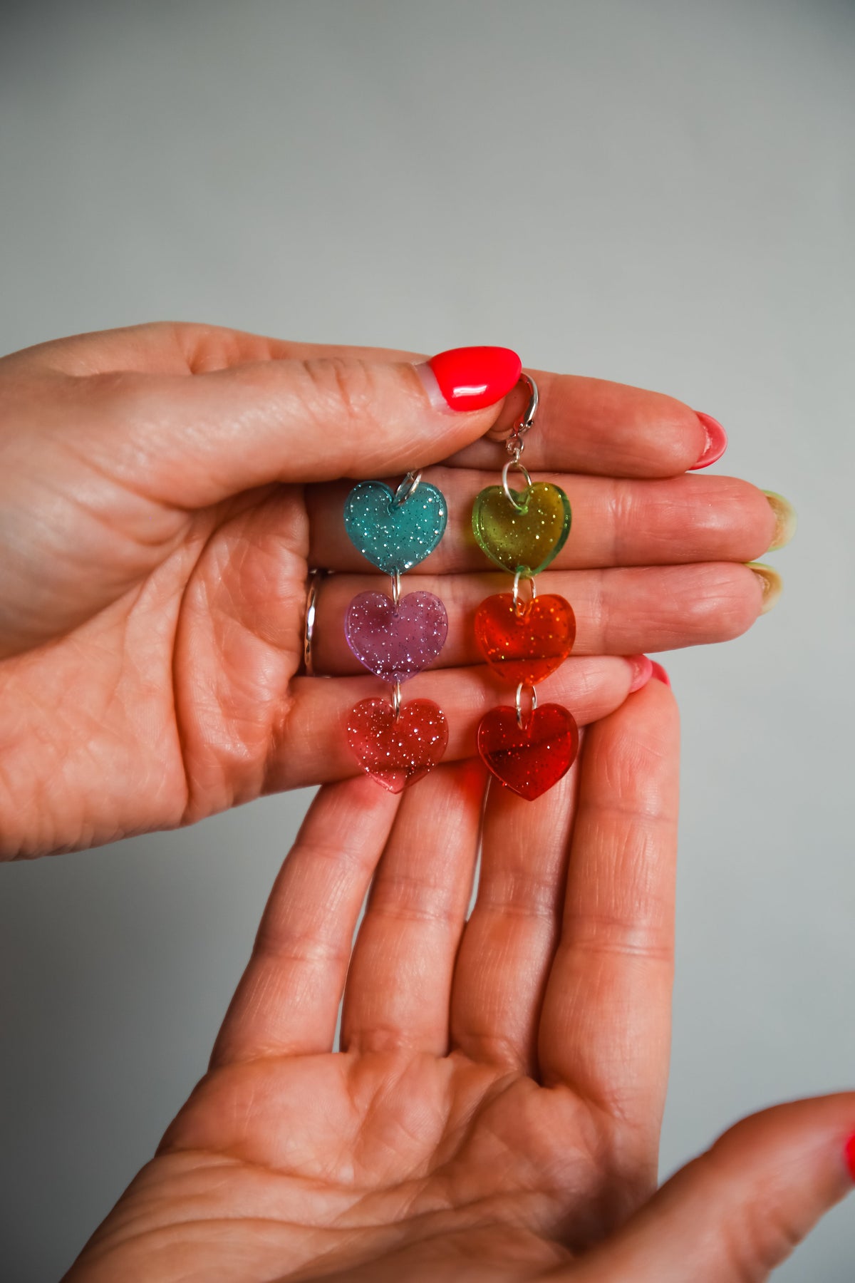 multi coloured heart acrylic earrings being held by hands