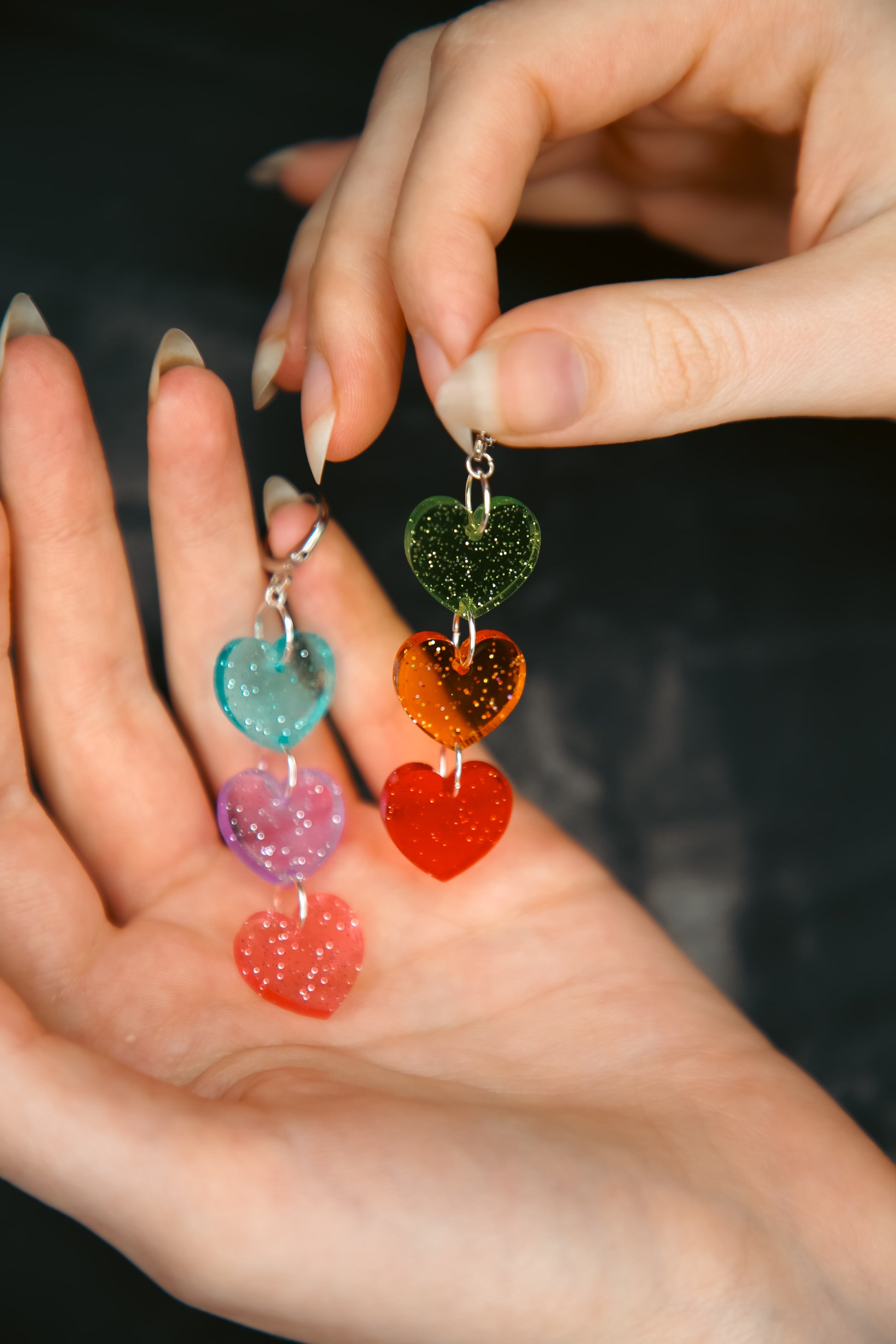 multi coloured heart acrylic earrings being held by hands