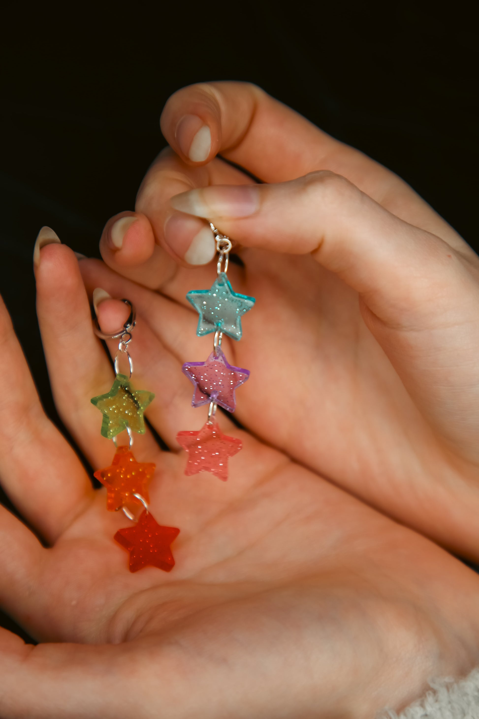 multicoloured glittery transparent star acrylic earring being held by hands