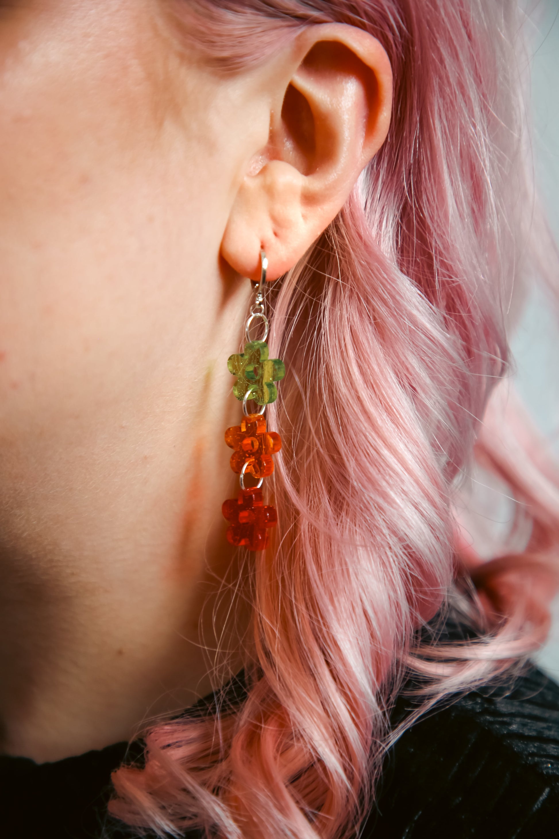 green, orange and red glittery transparent acrylic earring against pink hair