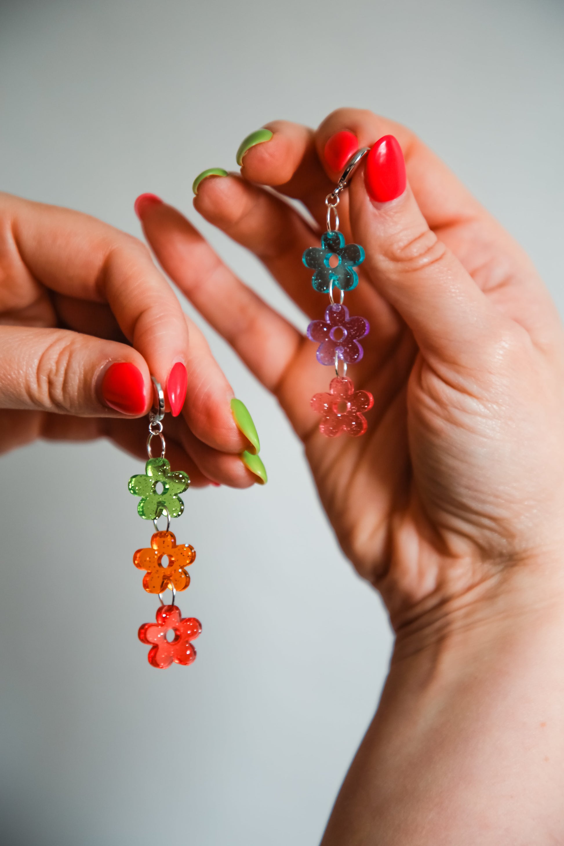 multi coloured flower acrylic earrings being held by hands