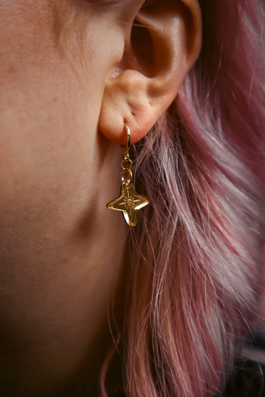 mini star shaped acrylic earring made from reflective gold acrylic against pink hair 