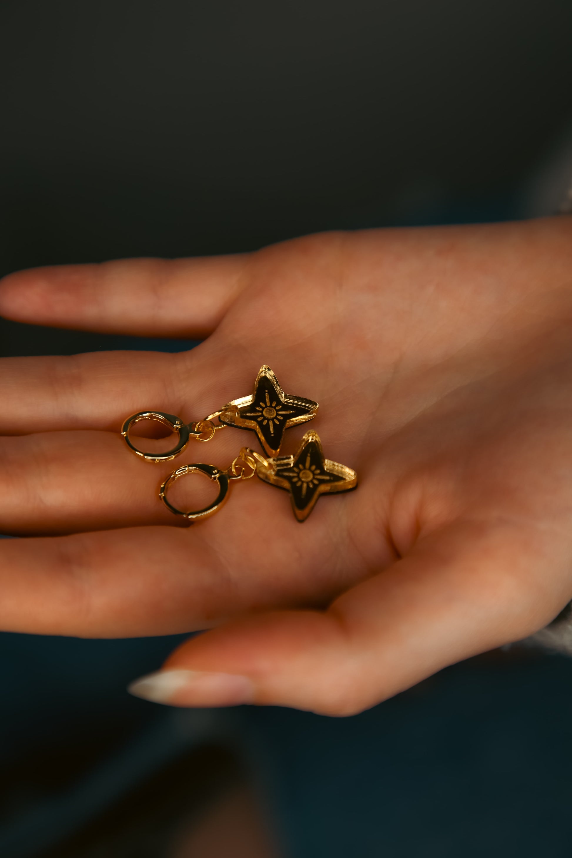 a pair of star shaped acrylic earring made from reflective gold acrylic being held by a hand
