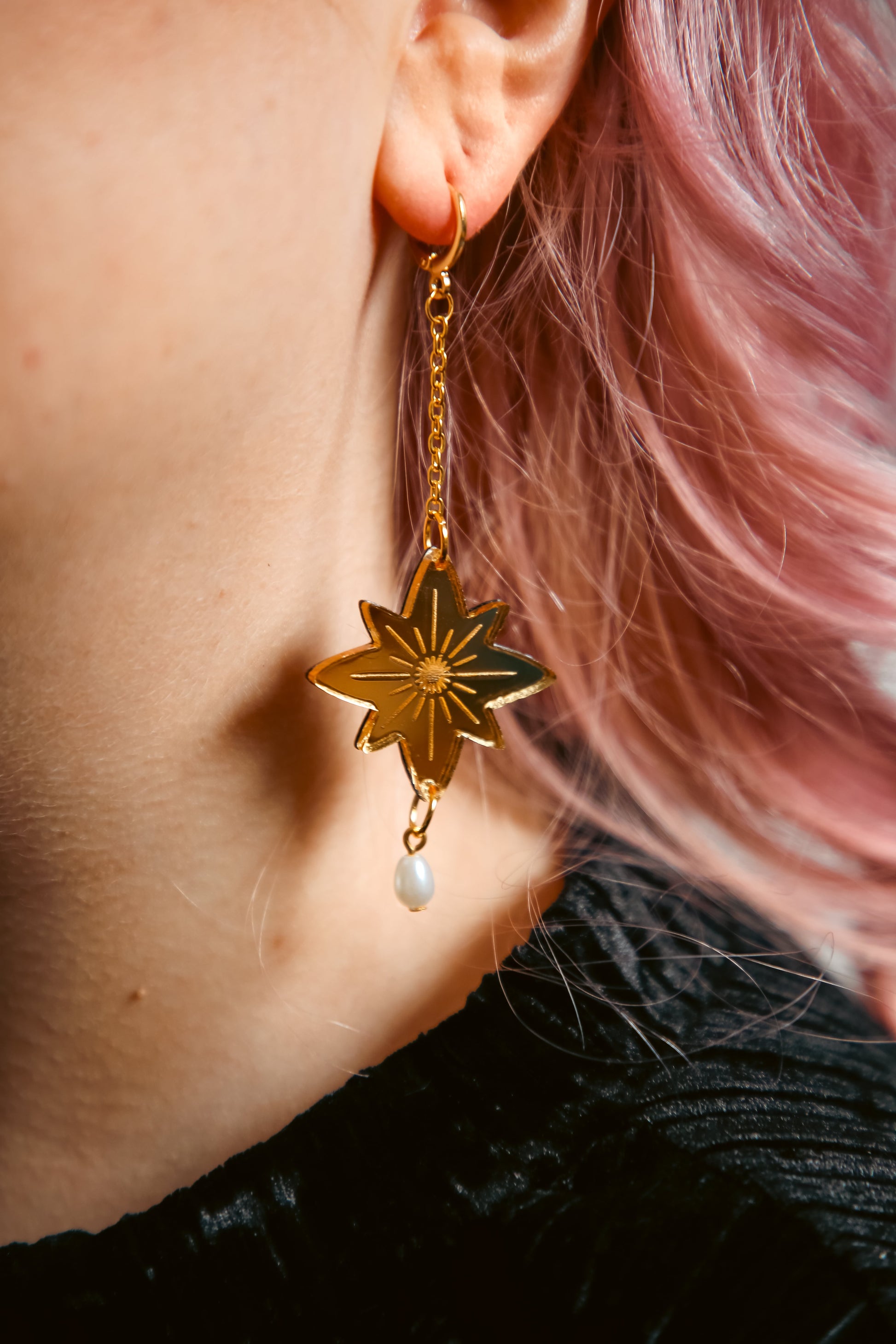 big star shaped acrylic earring made from reflective gold acrylic with a pearl dangling off against pink hair