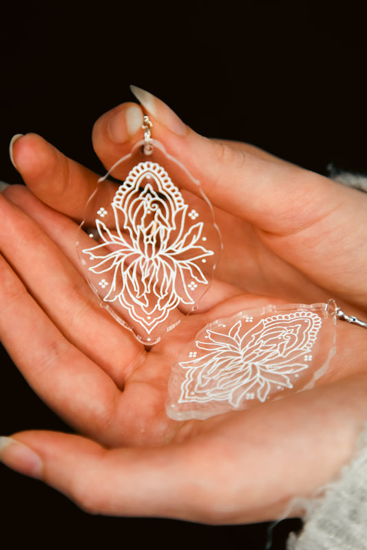 a pair of flower inspired acrylic earring made from transparent acrylic with a white being held by hands
