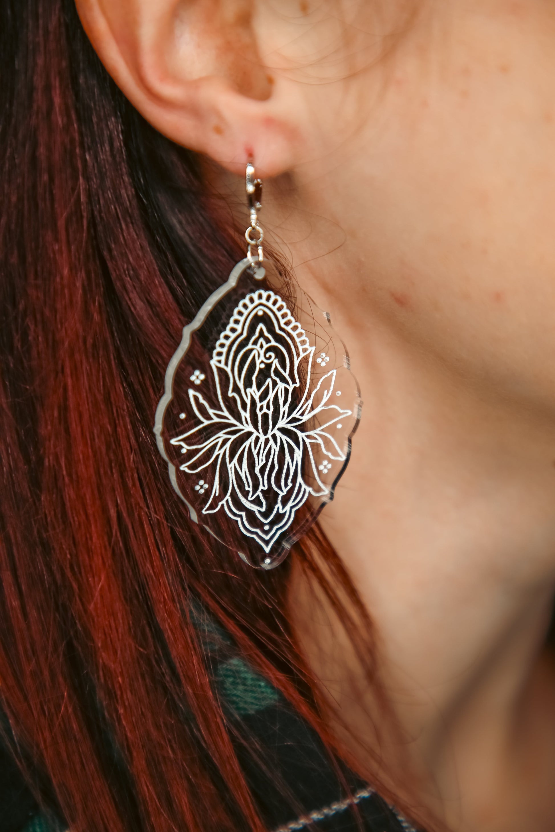 flower inspired acrylic earring made from transparent acrylic with a white design against brown hair