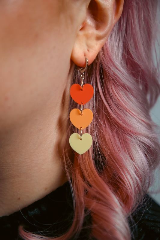 pastel dark orange, orange and yellow hearts acrylic earring against pink hair