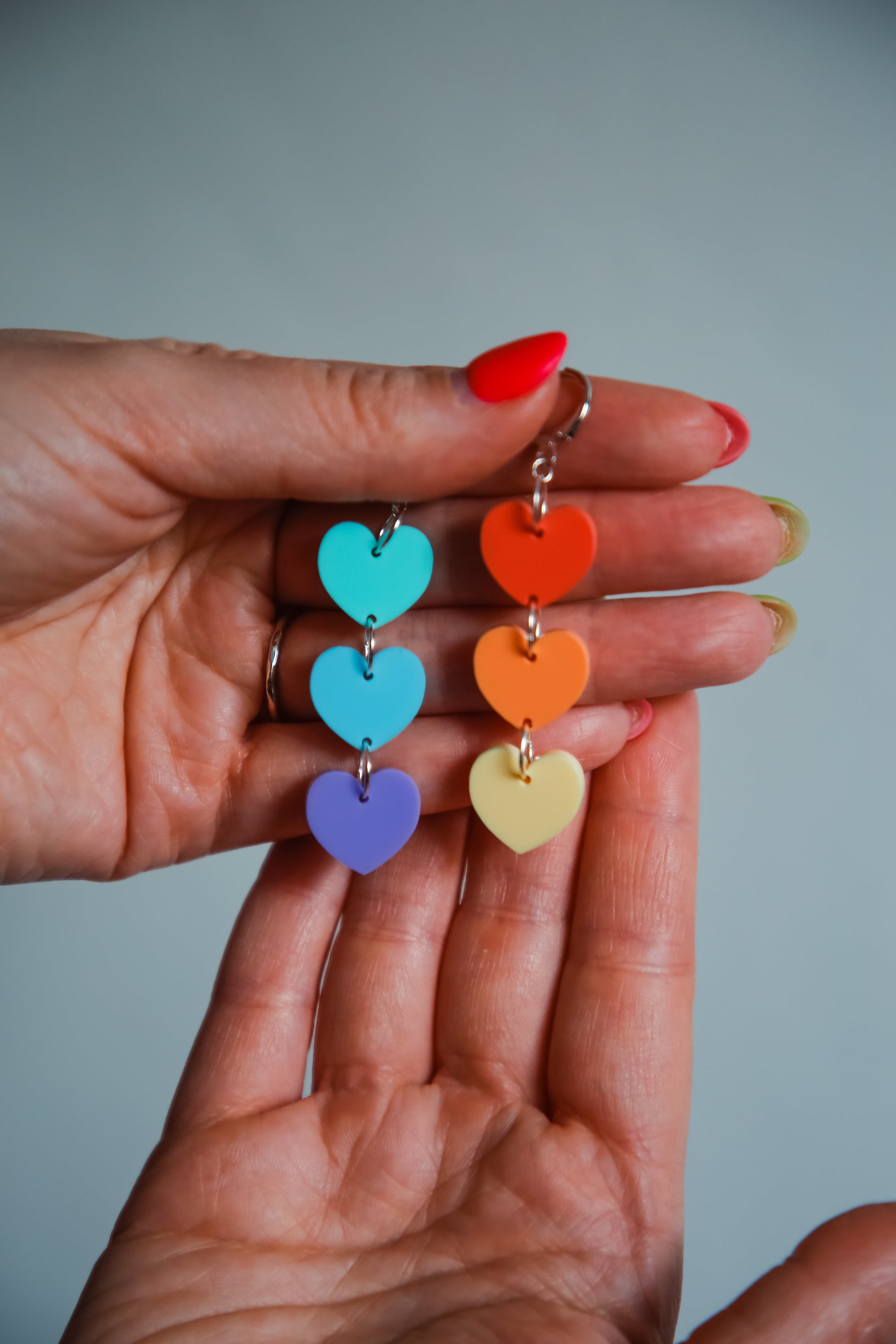 multicoloured pastel heart shaped acrylic earrings being held by hands