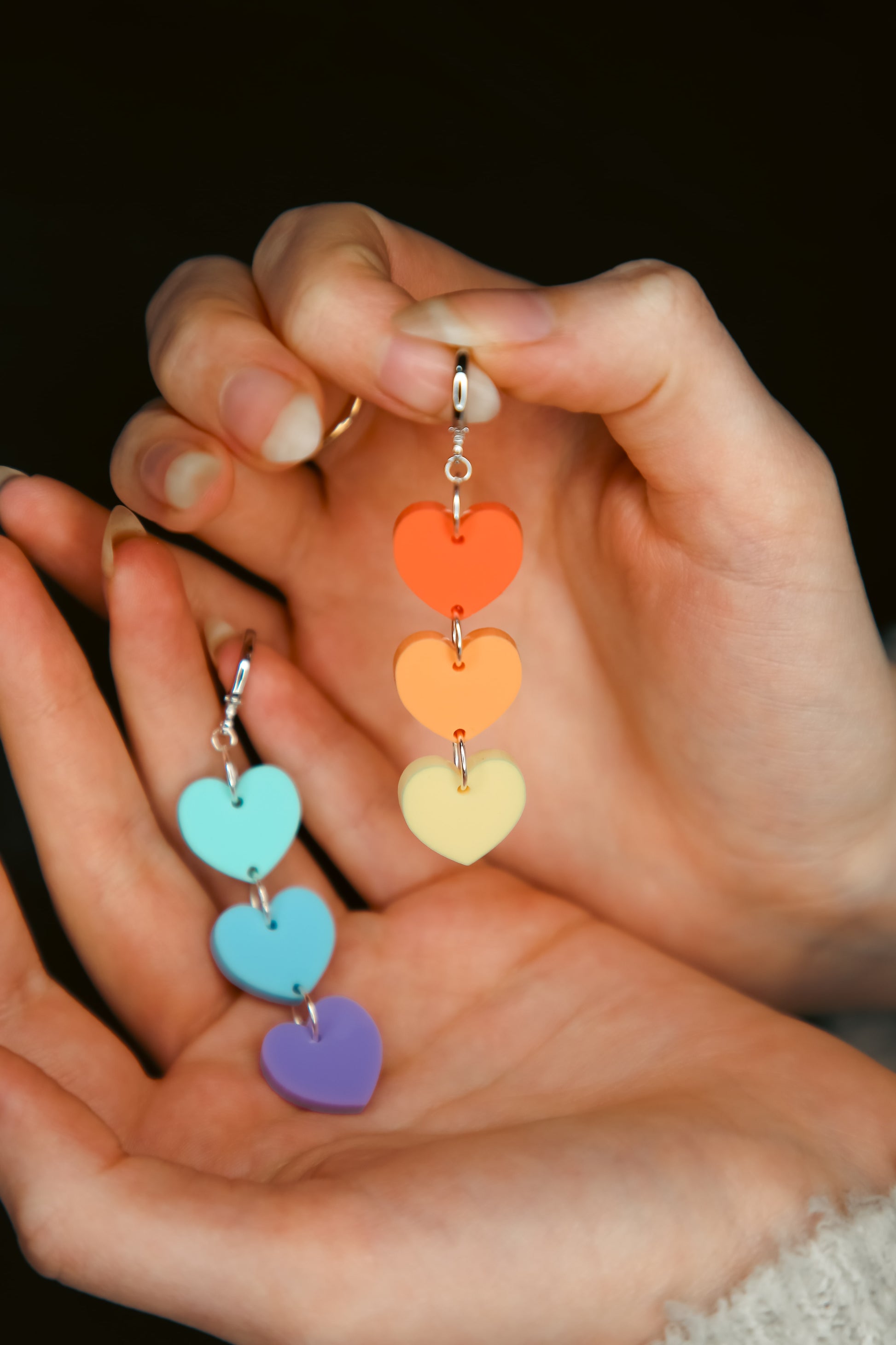 multicoloured pastel heart shaped acrylic earrings being held by hands