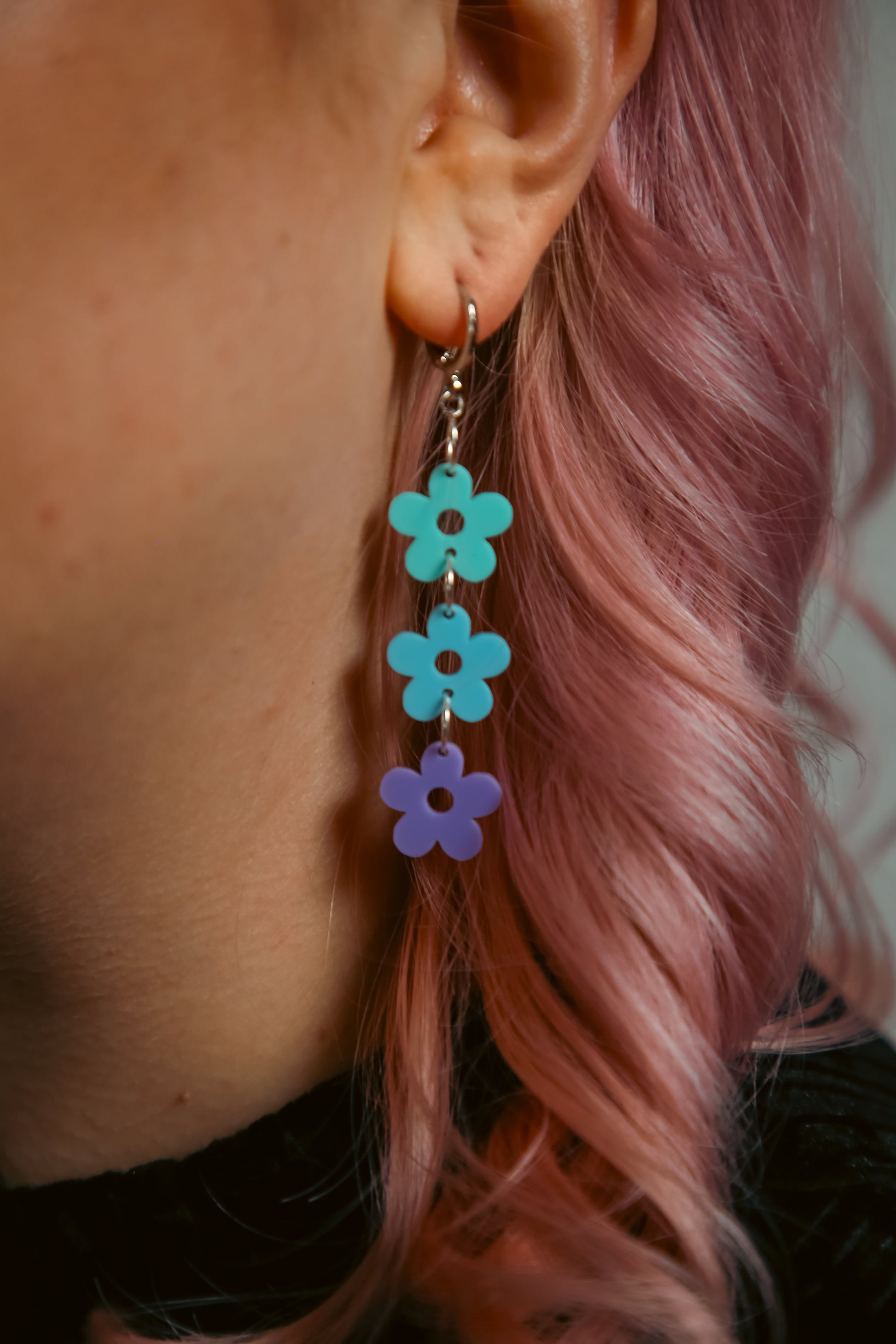 pastel cyan, blue and purple flower shaped acrylic earrings against pink hair