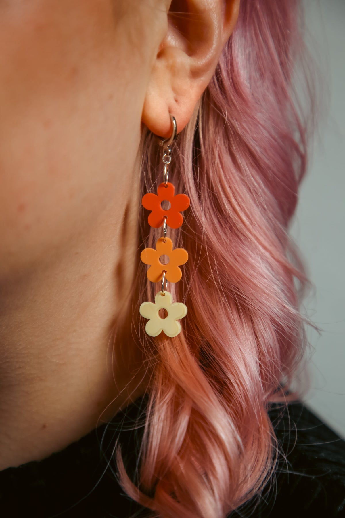 pastel dark orange, orange and yellow flower shaped acrylic earrings against pink hair