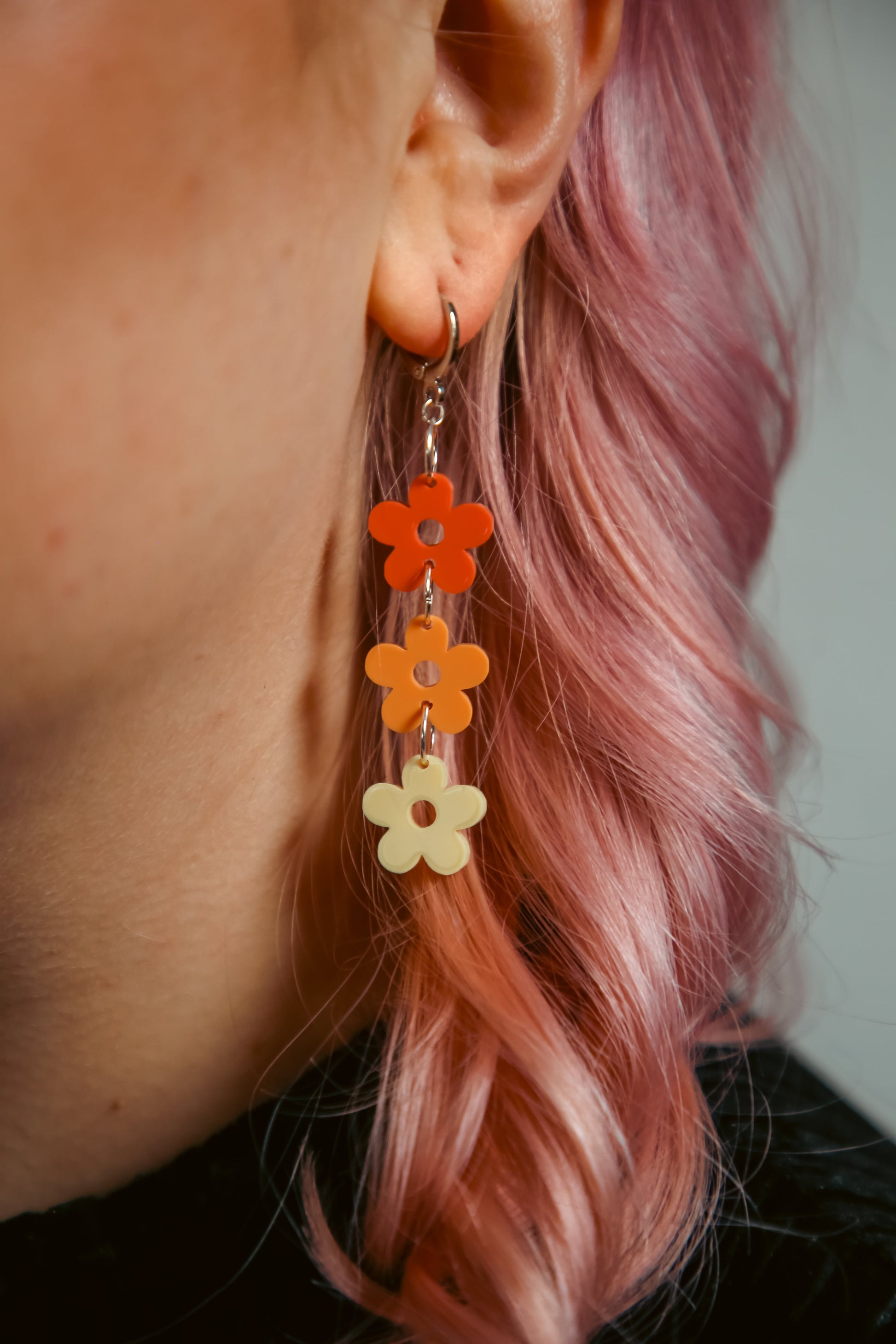 pastel dark orange, orange and yellow flower shaped acrylic earrings against pink hair