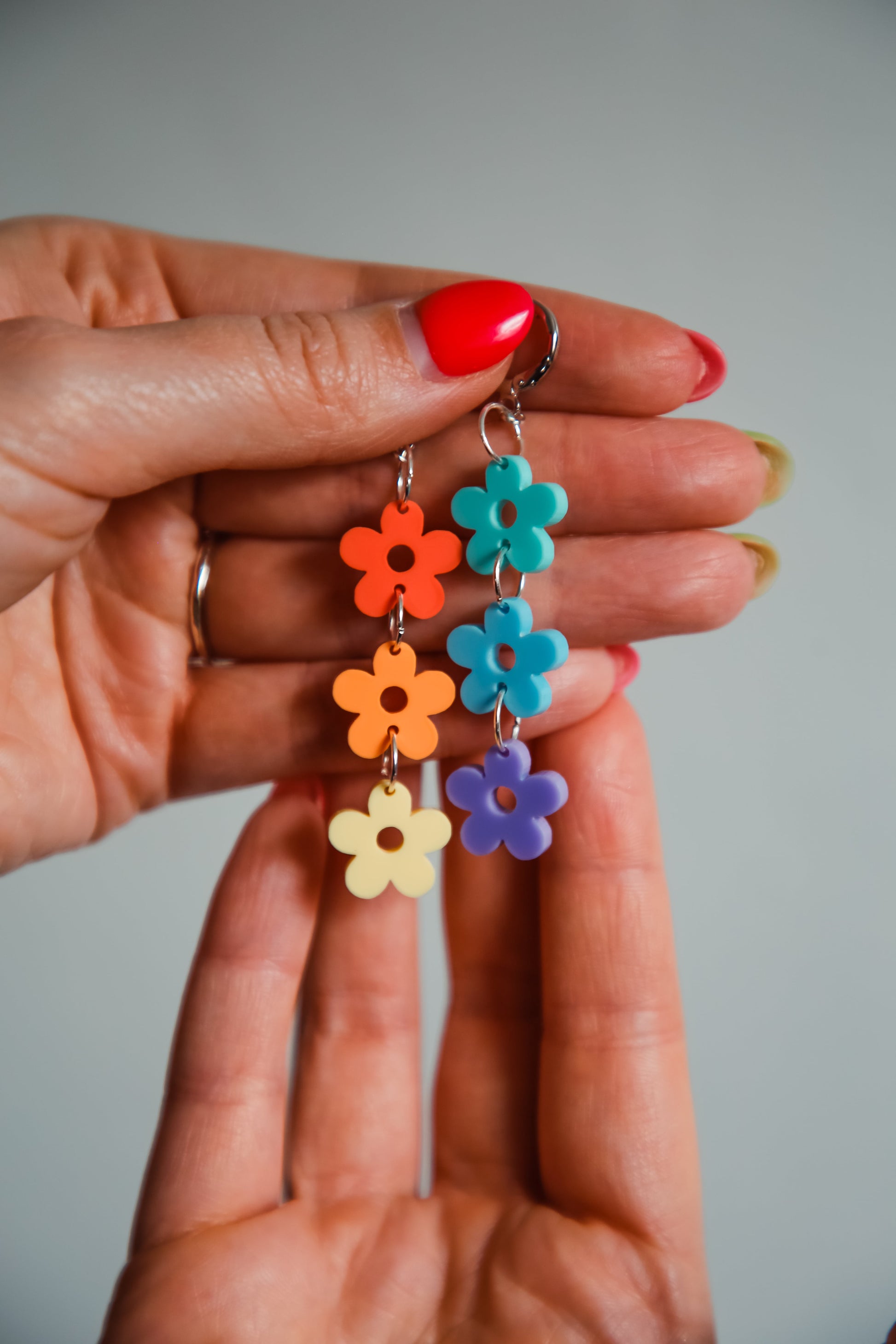 multi coloured pastel flower acrylic earrings being held by a hand