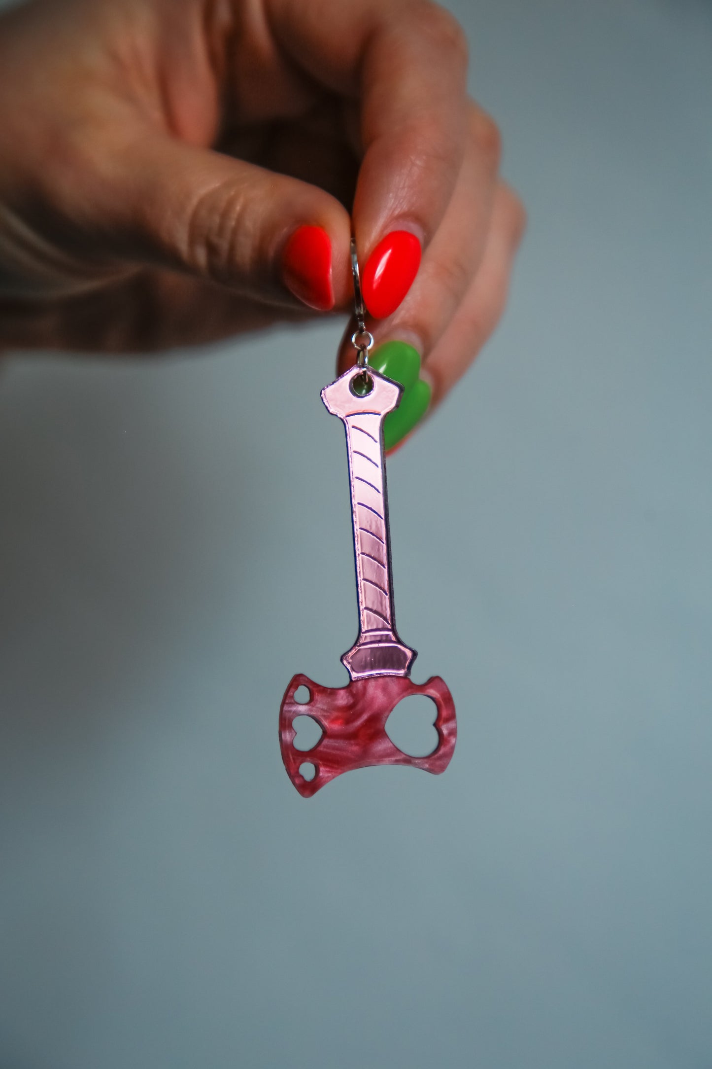 axe acrylic earring with pink blade and reflective pink handle being held by a hand